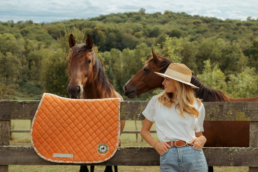 Photographie d'un tapis de selle cousu main, devant un cheval et sa cavalière.