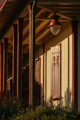 Gros plan sur la façade d'une maison en bois aux volets fermés, avec des piliers rouges et une lampe extérieure vintage.