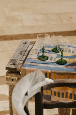 Gros plan sur trois verres à pied transparents au pied vert texturé, posés sur une nappe jacquard Tissage Moutet.