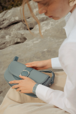 Gros plan sur les mains d'un mannequin ouvrant le sac en cuir bleu Ainhoa de la maison de maroquinerie basque Erro.