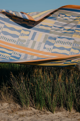 Pièce de linge de maison Tissage Moutet aux motifs graphiques bleus et jaunes flottant au-dessus des herbes de la dune.